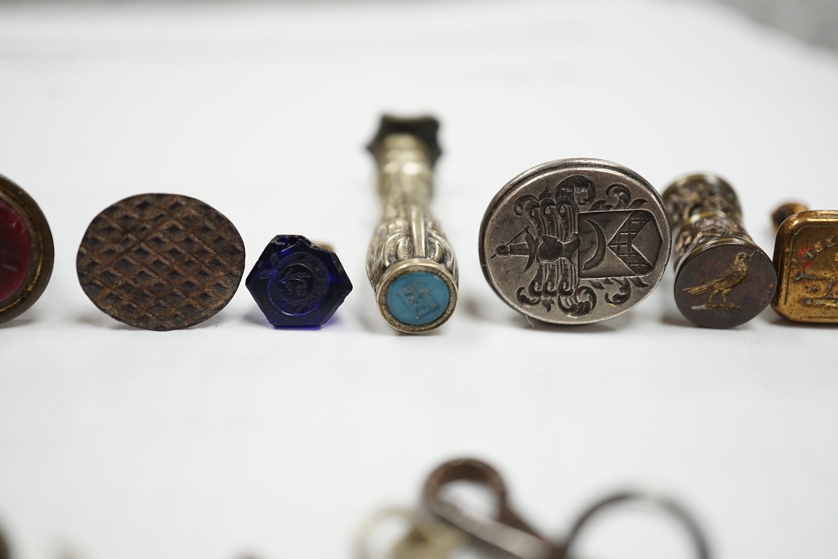 A group of twenty-five steel, gilt metal or nickel fob or desk seals, mostly 19th-century, including a steel swivel seal, a seal with boxwood finial modelled as a hand holding a ball and a nickel multi seal